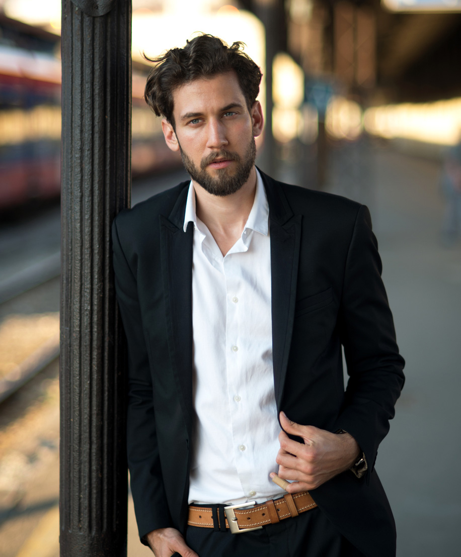 man in black suit leaning against a pole - FUE hair transplant in NYC